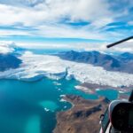 Hubschrauber fliegt über Eisformationen und blaues Wasser.