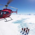 Helicopter flying over icy terrain with adventurers below.