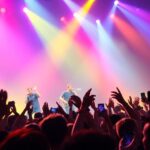 Concert avec des fans et un groupe sous des lumières de scène colorées.