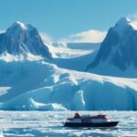 Expeditionsschiff in der eisigen Antarktislandschaft unter blauem Himmel.