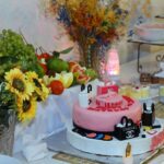 a table topped with a pink cake next to a bowl of fruit