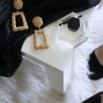 pair of gold-colored earrings on table and black ankle-strap pumps on area rug