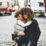 photography of woman carrying baby near street during daytime