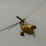 a yellow helicopter flying through a cloudy sky