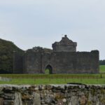 a stone building with a fence and trees in the background