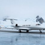 Private jet on blue ice runway in Antarctica with mountains.